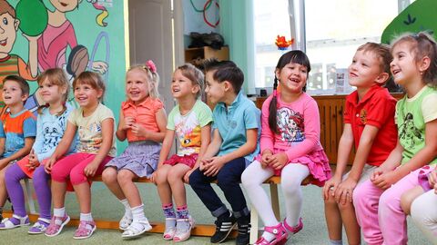 viele Kindergartenkinder sitzen vor einer bunten Wand auf einer Bank