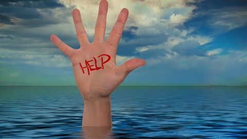 Hand ragt aus dem Meer mit Help Schriftzug an der Innenfläche