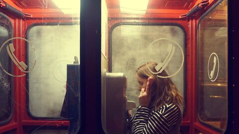 Frau in einer roten Telefonzelle hält den Hörer ans Ohr